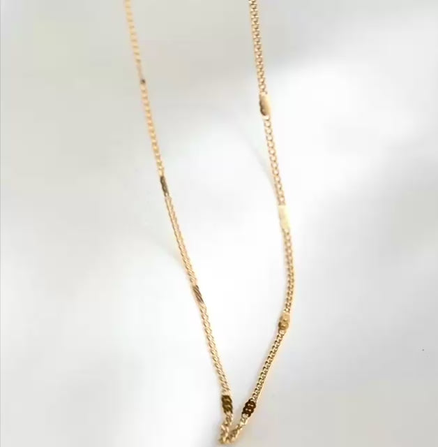 Ultra thin gold curb chain with flat rectangular beads stationed along, reflecting light as the chain moves.