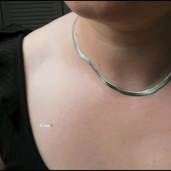 4mm silver herringbone necklace in 16 inches on a woman wearing a black blouse, the necklace catching and reflecting light as the model moves.