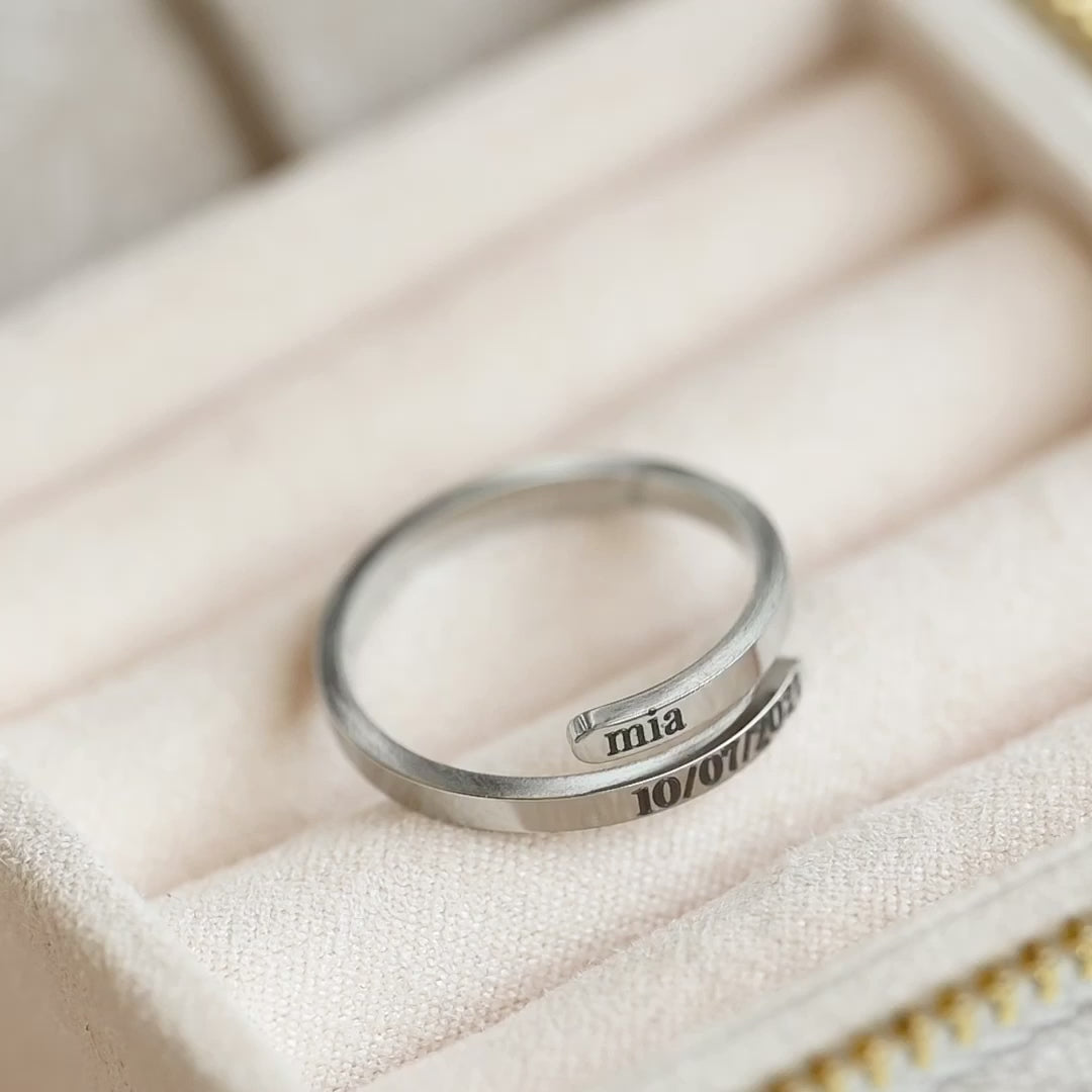 Top view of an engraved silver wrap ring with bypass design, the top flat and high polished side is reflecting light as the reflector moves.