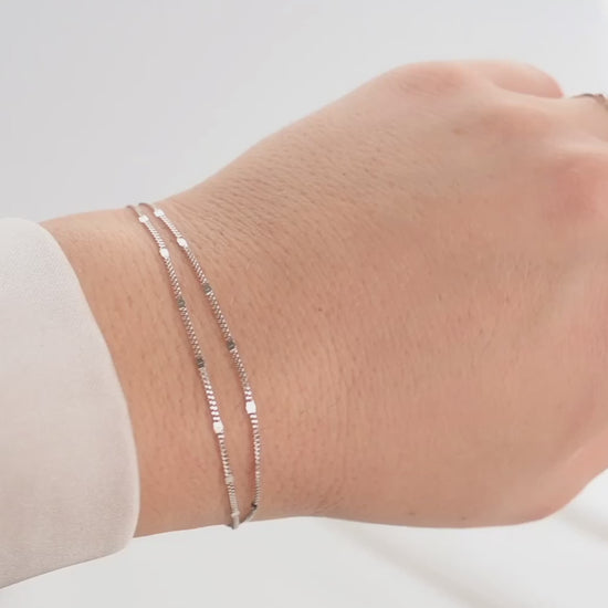 Silver double layered chain bracelet with shimmering sequins on a wrist against white background.