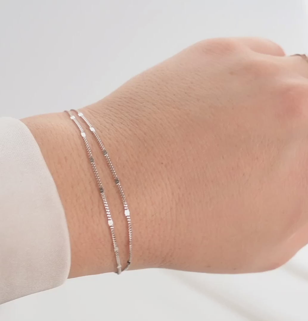 Silver double layered chain bracelet with shimmering sequins on a wrist against white background.