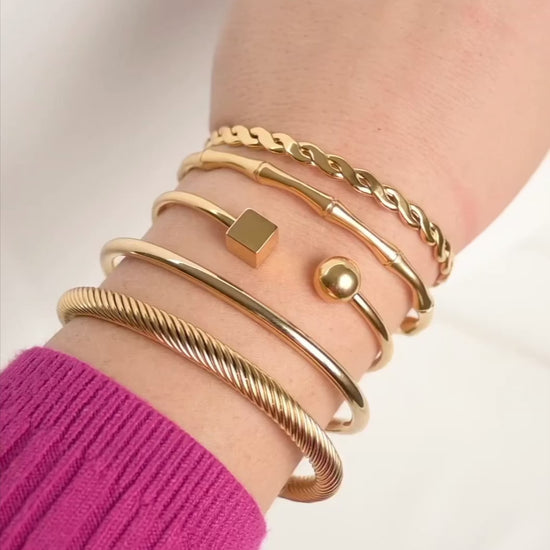 Stack of gold open bangles on a wrist, with bracelets reflecting light as the model moves her wrist.