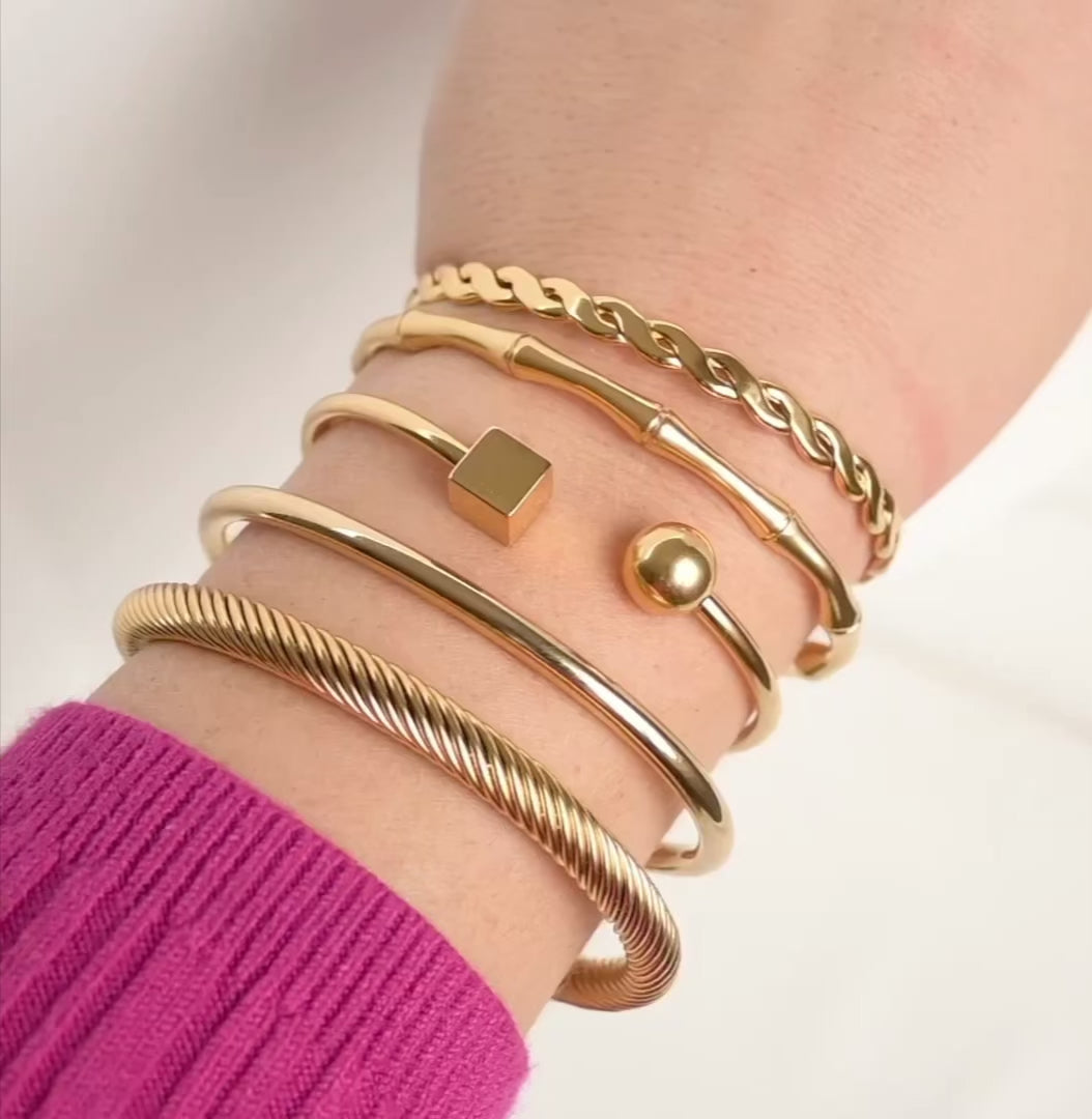 Stack of gold open bangles on a wrist, with bracelets reflecting light as the model moves her wrist.