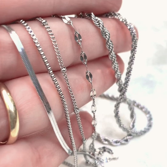 Stainless steel chain bracelets with high-polish silver-tone in hand, with chains reflecting light as the hand moves.