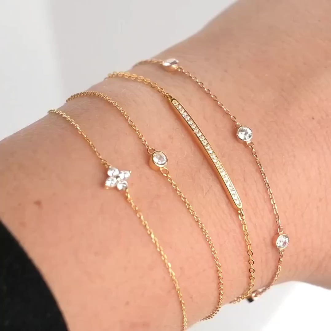 A stack of gold clover, bezel, pave bar, and bezel station bracelets with cubic zirconia, the stones and 925 silver chains sparkling as the hand moves.