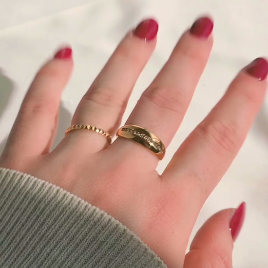Chunky gold CZ dome ring stacked on fingers with a dainty geometric band, metal reflecting light and stones sparkling as the hand with red nail polish moves.