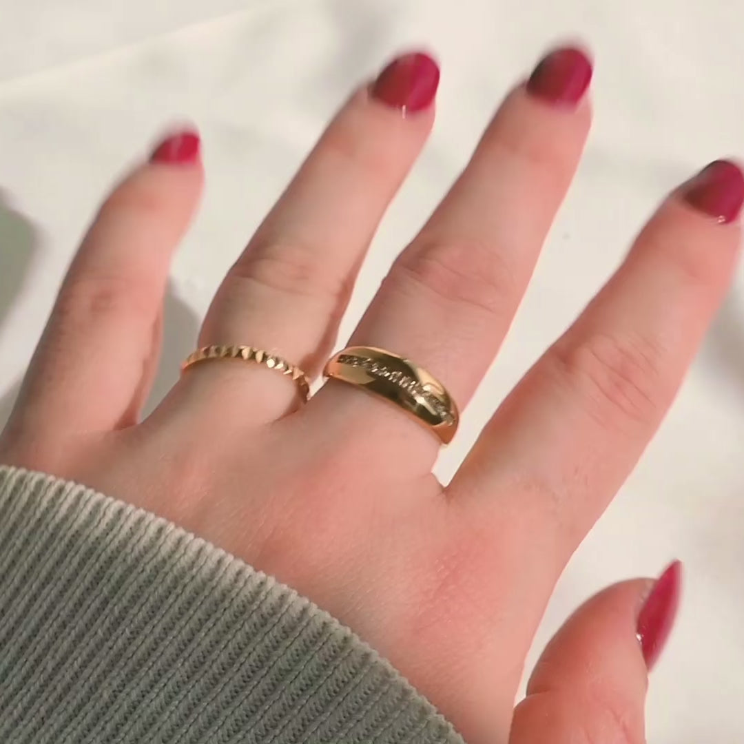 Chunky gold CZ dome ring stacked on fingers with a dainty geometric band, metal reflecting light and stones sparkling as the hand with red nail polish moves.