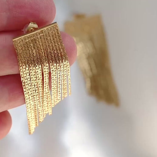 Gold chain tassel earrings in hand reflecting light as it moves