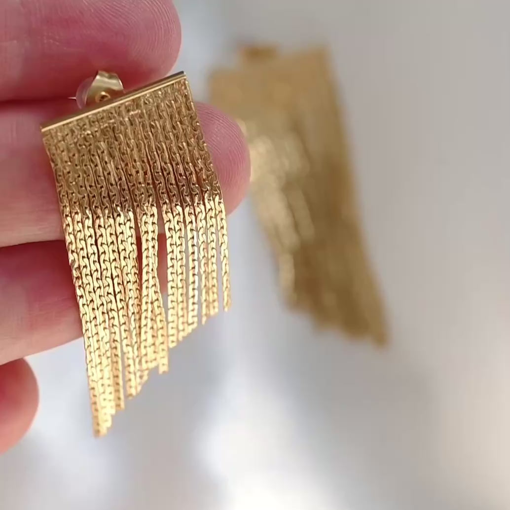Gold chain tassel earrings in hand reflecting light as it moves