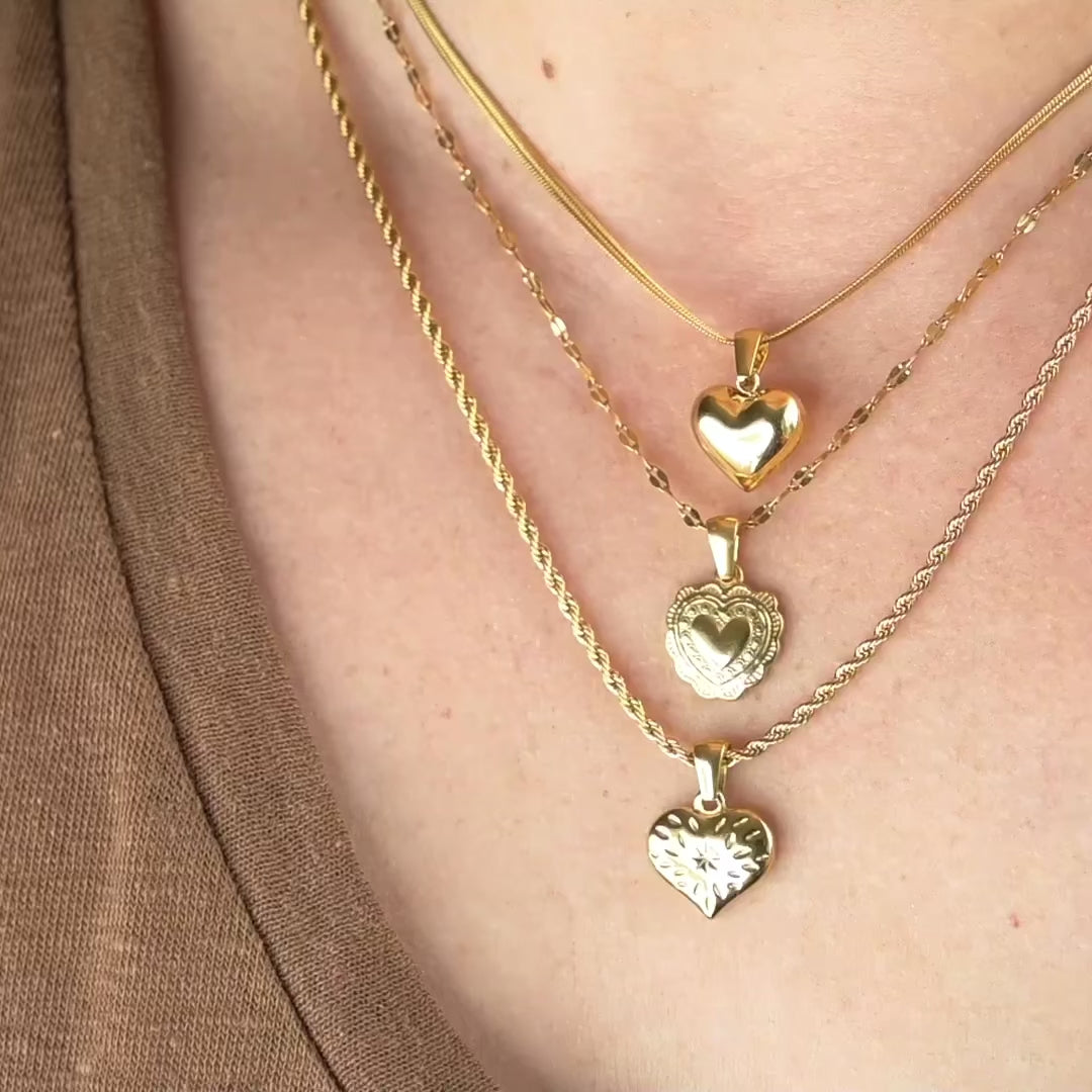 woman showing the gold heart pendants from different angles as chain and pendants shimmer as they catch light.