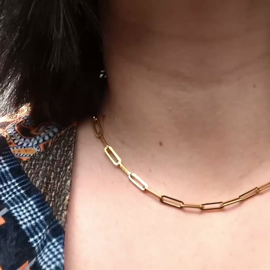 Thick gold paperclip chain choker on a persons neck, links sparkle as they catch light when model moves.