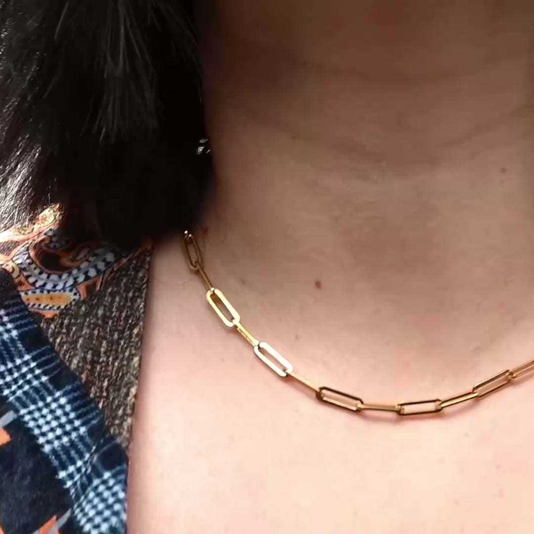 Thick gold paperclip chain choker on a persons neck, links sparkle as they catch light when model moves.