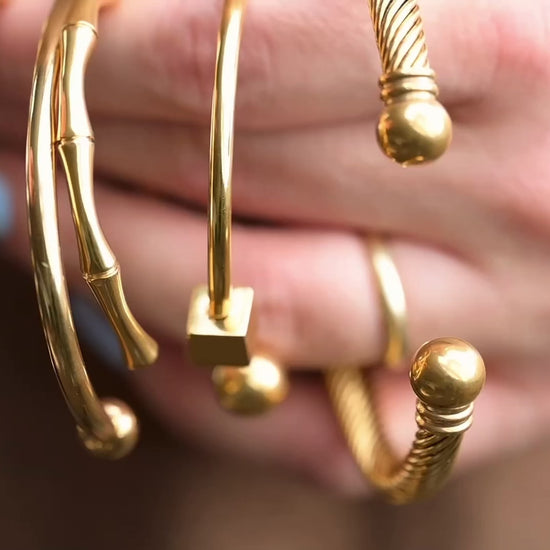5 different cuf bracelets held by a hand, reflecting light as the hand moves