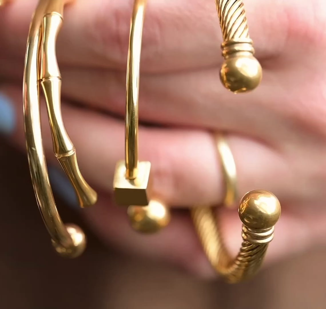 5 different cuf bracelets held by a hand, reflecting light as the hand moves