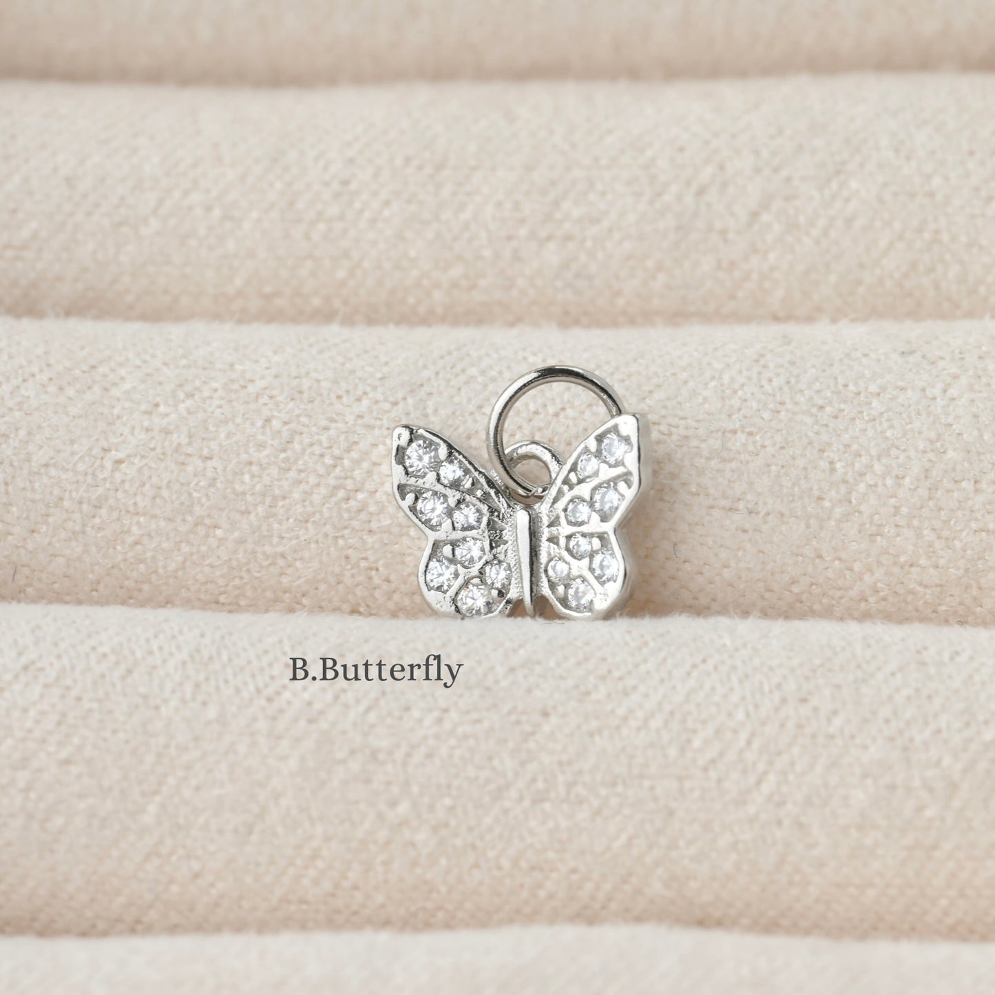 Butterfly-shaped silver charm with clear stones on a beige fabric background