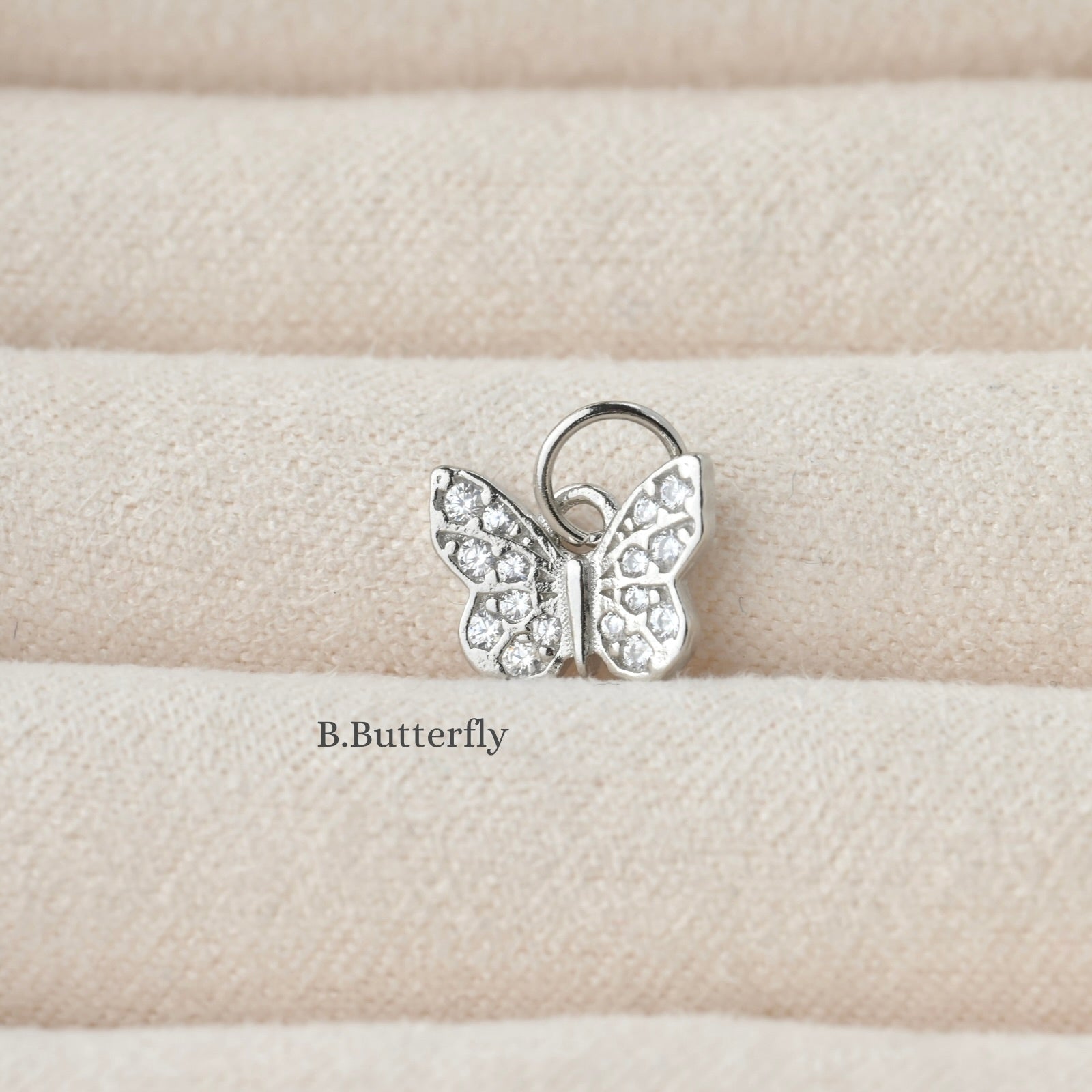 Butterfly-shaped silver charm with clear stones on a beige fabric background