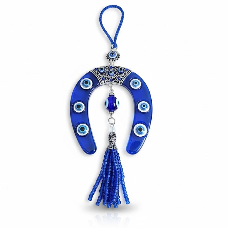 Blue horseshoe-shaped decorative item with tassel and evil eye designs on a white background