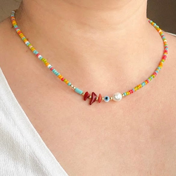 Colorful seed bead necklace with a white pearl and natural red stones on a person wearing a white top.