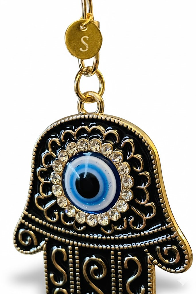 Close-up view of the evil eye and tiny disc charm with letter 'S' on decorative fatima's hand keychain 