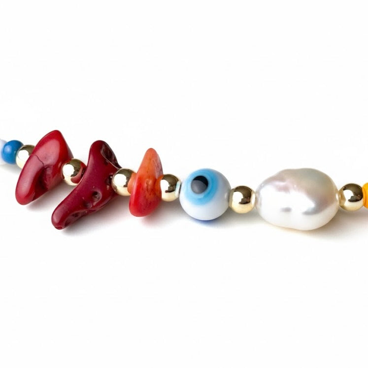 Close-up view of the three natural red agate stones, a round white evil eye bead and a freswater pearl each seperated with gold beadson a white background