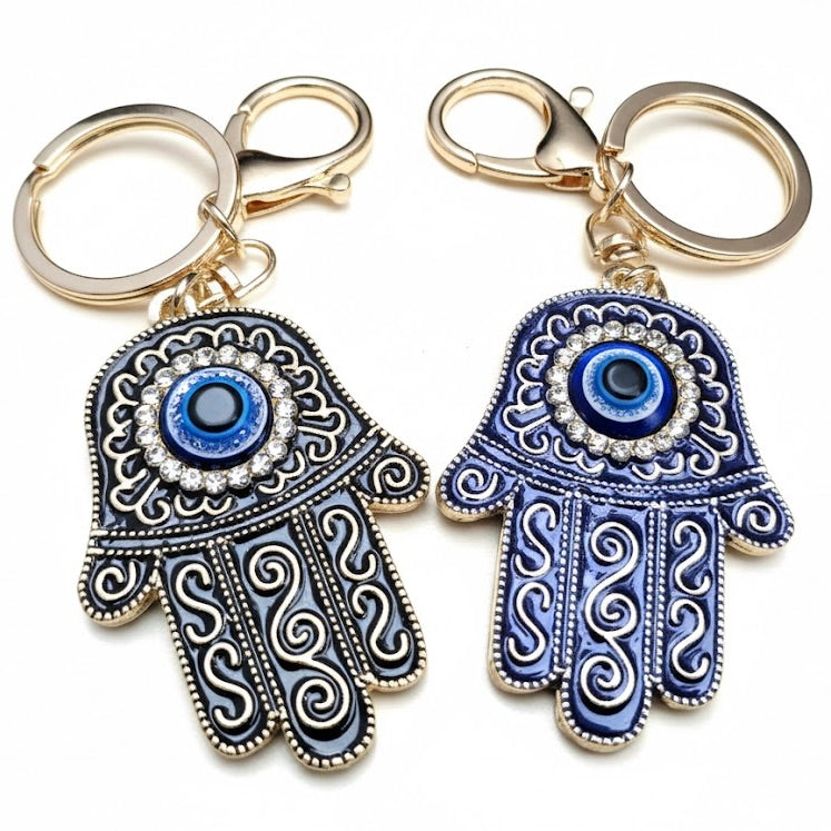 One black and one blue Hamsa hand keychains with evil eye design on a white background