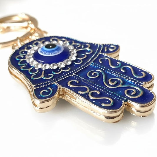 Blue Hamsa hand keychain with gold accents and evil eye on a white background