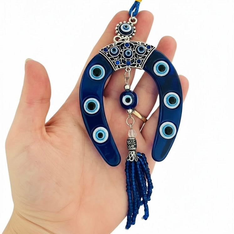 Blue evil eye charm with tassel held in a hand against a white background