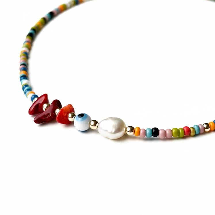Close up view of colorful beaded evil eye necklace with a pearl and stones on a white background