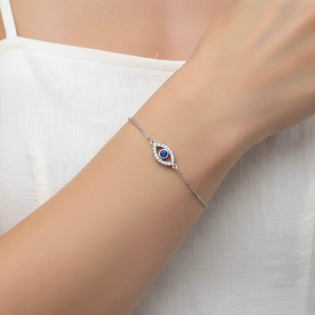 Silver evil eye bracelet with a dark blue stone centerpiece and clear crystal inlays around, on a wrist against a white background