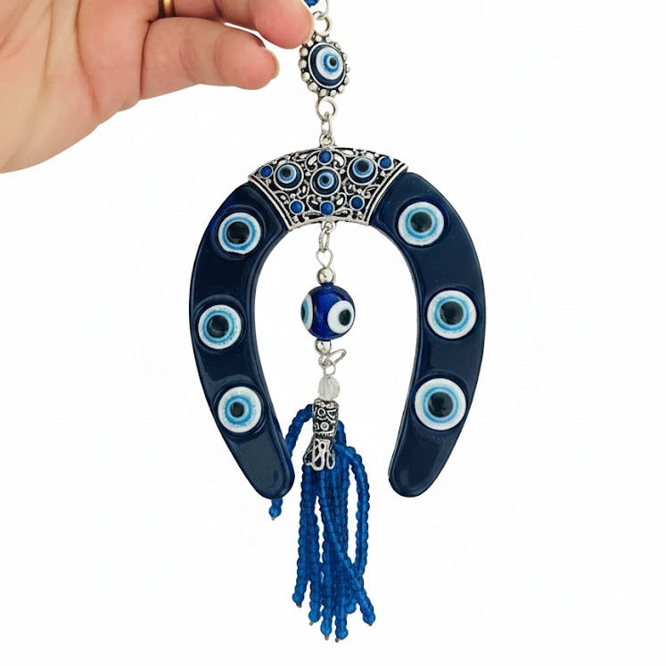 Hand holding a horseshoe evil eye object with tassels on a white background