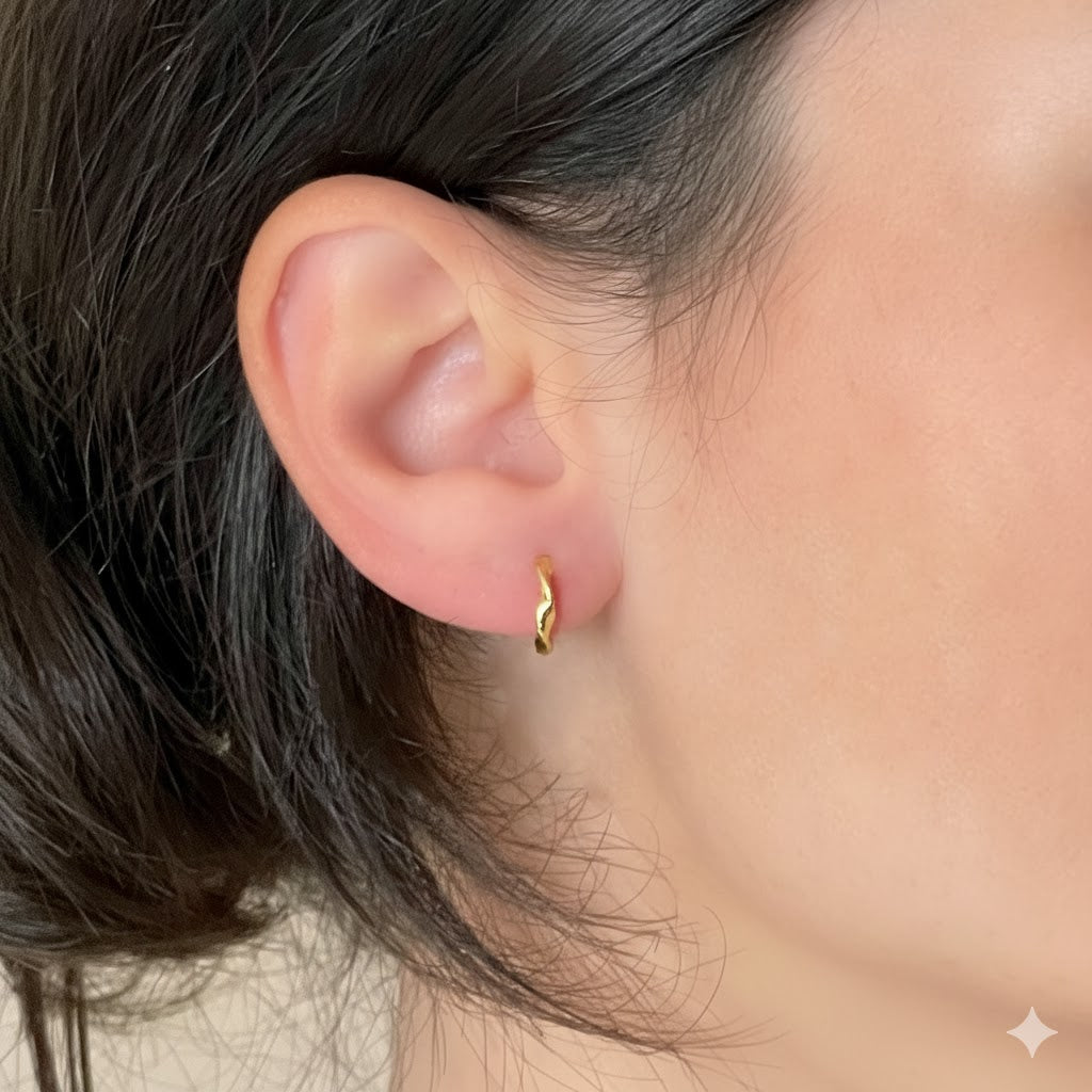 Close-up of an ear wearing tiny gold twisted hoop earrings 
