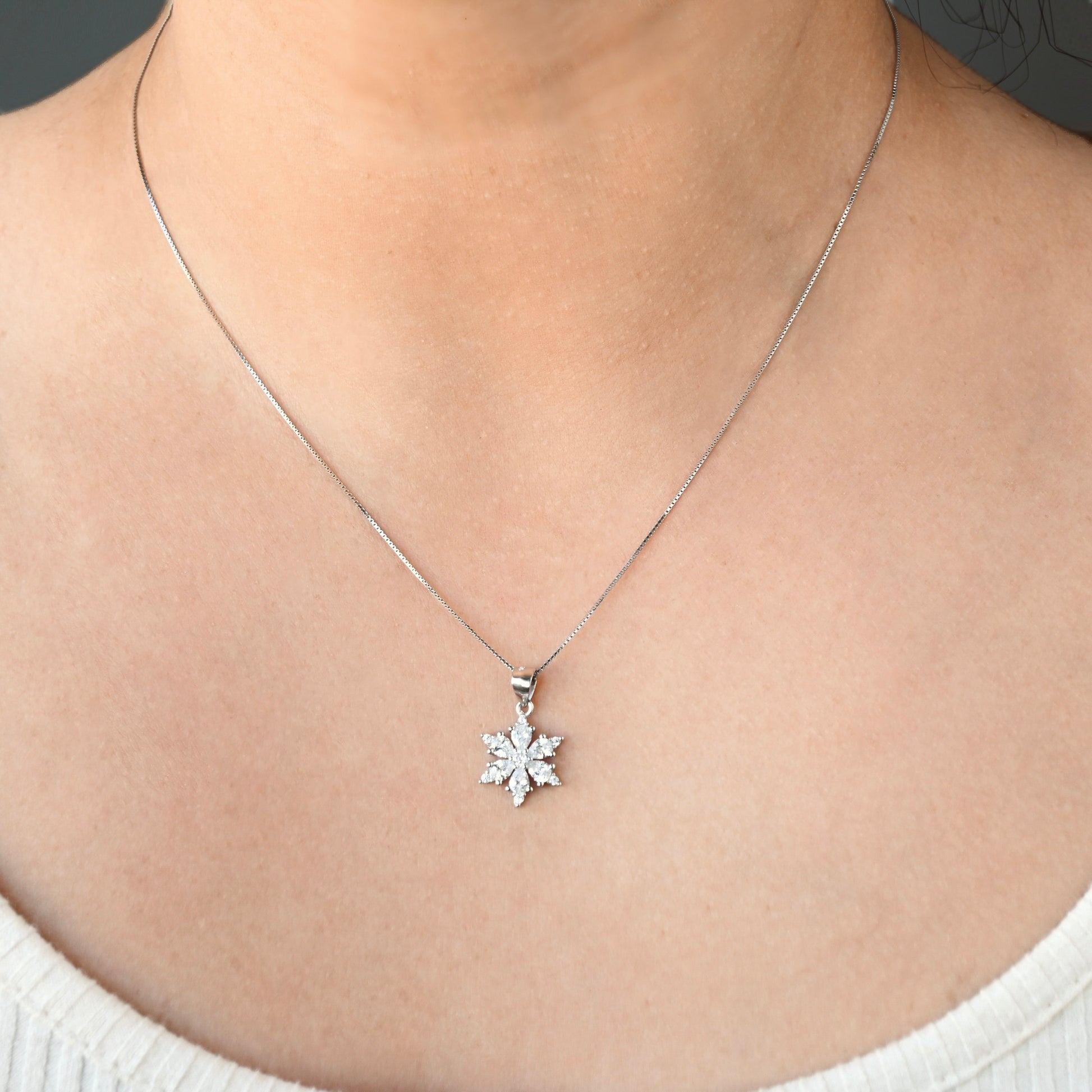 Silver necklace with a snowflake pendant on a thin box chain on a person's neck