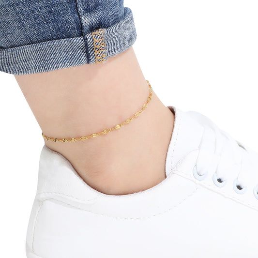 Gold sequin chain anklet on a person's ankle with a white shoe and blue jeans in the background