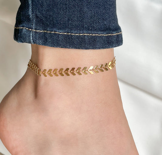 Gold chevron link anklet with high-polish finish worn on an ankle with denim