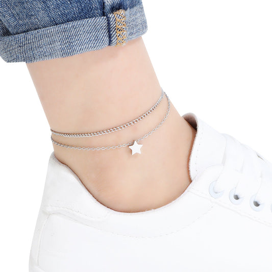 Two layered silver anklet with star charm on a person's ankle against a white background